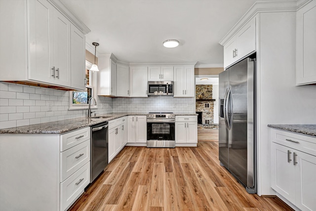 kitchen featuring stainless steel appliances, decorative backsplash, white cabinetry, a sink, and light stone countertops