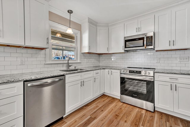 kitchen featuring stainless steel appliances, decorative backsplash, white cabinets, a sink, and light wood-type flooring