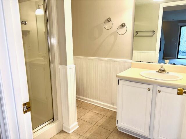 bathroom with a stall shower, wainscoting, wooden walls, vanity, and tile patterned flooring