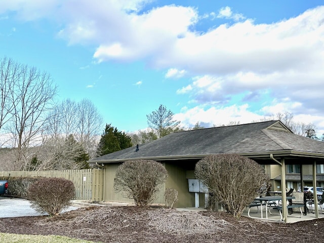 rear view of property with a shingled roof, a patio area, fence, and stucco siding