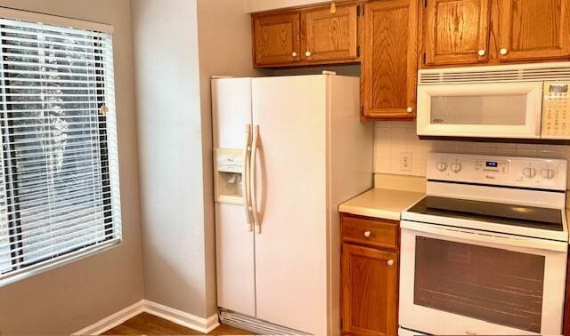 kitchen with light countertops, backsplash, brown cabinetry, white appliances, and baseboards