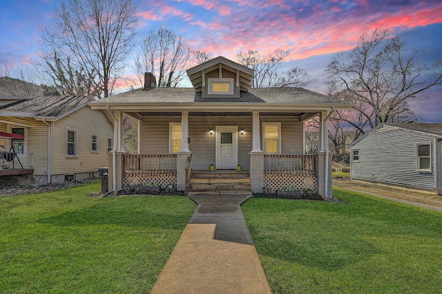 bungalow-style house with a porch, a yard, and a shingled roof