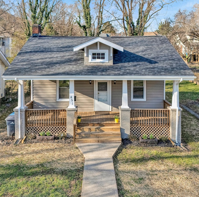 bungalow-style home featuring a chimney, covered porch, and a shingled roof