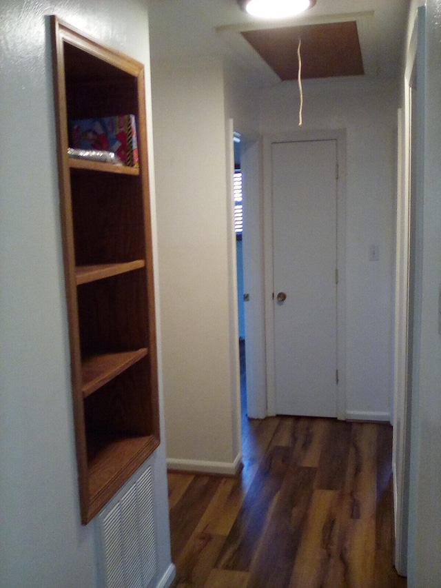 hallway featuring attic access, visible vents, baseboards, and wood finished floors