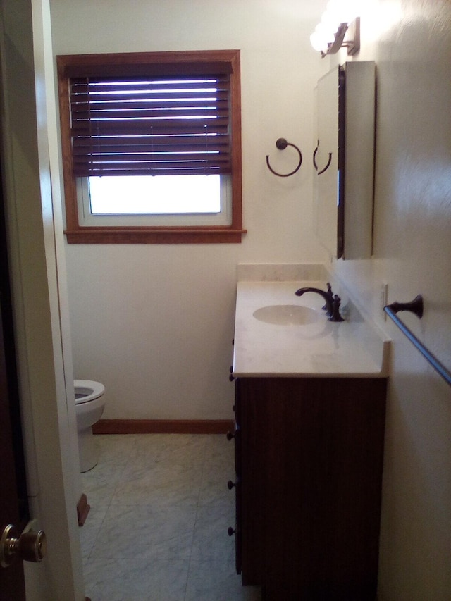 half bathroom featuring toilet, baseboards, and vanity