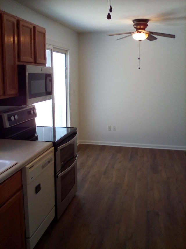 kitchen with dark wood-style floors, brown cabinets, appliances with stainless steel finishes, ceiling fan, and baseboards