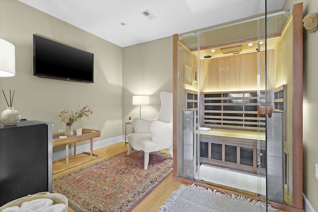 living area with a sauna, wood finished floors, visible vents, and baseboards