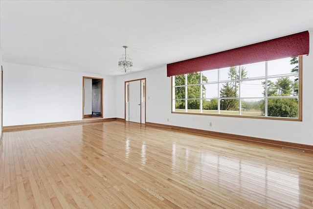 spare room featuring light wood finished floors, visible vents, baseboards, and an inviting chandelier