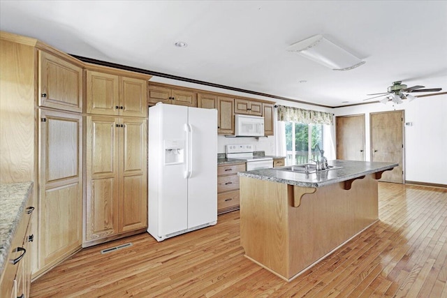 kitchen with white appliances, a kitchen bar, light wood finished floors, and a sink