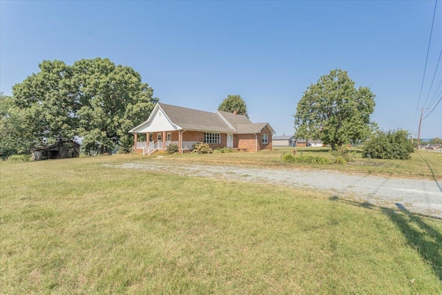 view of front of home featuring gravel driveway, covered porch, brick siding, and a front lawn