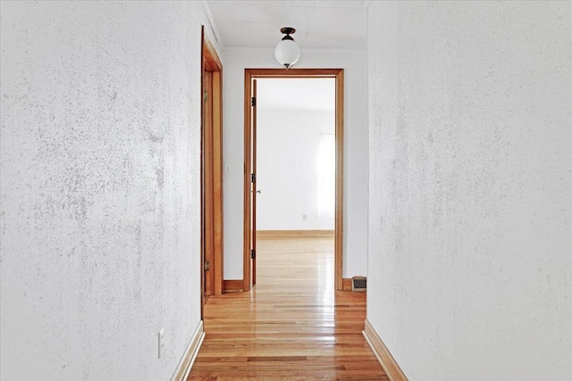 hallway featuring visible vents, light wood-style flooring, and baseboards