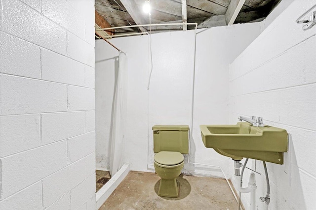 bathroom with concrete block wall, concrete floors, toilet, and walk in shower