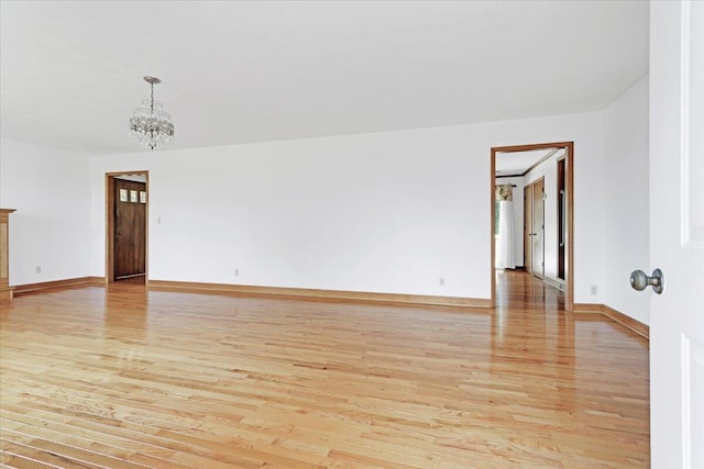 empty room featuring baseboards, light wood-type flooring, and a notable chandelier