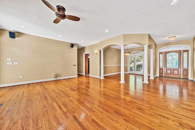 interior space featuring light wood-style floors, arched walkways, baseboards, and ornate columns