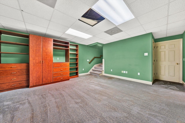 below grade area featuring carpet, a paneled ceiling, stairway, and baseboards