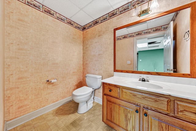 bathroom with baseboards, a drop ceiling, toilet, tile patterned floors, and vanity