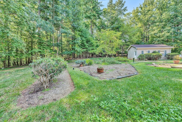 view of yard featuring a vegetable garden, a wooded view, and an outbuilding