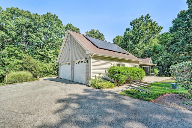 view of home's exterior with roof with shingles, a detached garage, and solar panels