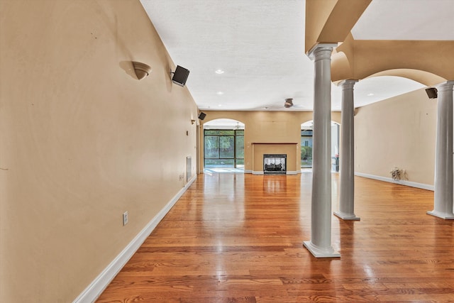 unfurnished living room with ornate columns, a fireplace, arched walkways, and wood finished floors