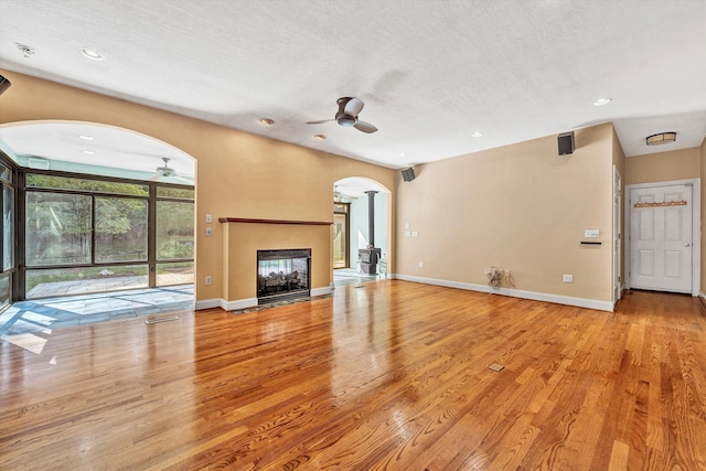 unfurnished living room featuring arched walkways, wood finished floors, a multi sided fireplace, and baseboards