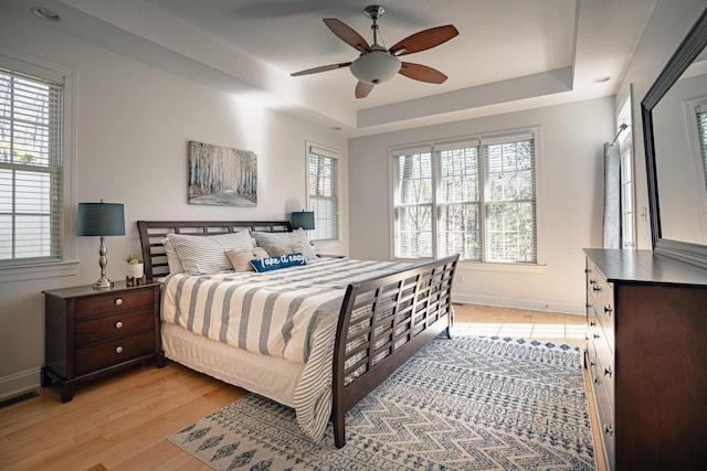 bedroom featuring light wood-type flooring, a tray ceiling, visible vents, and baseboards