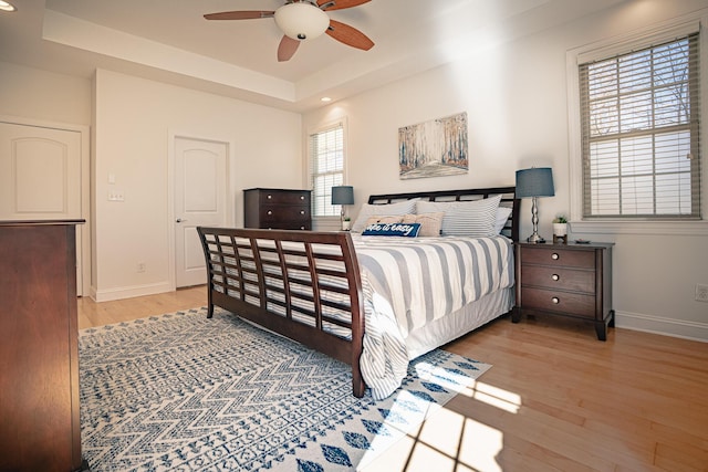 bedroom featuring light wood finished floors, ceiling fan, baseboards, and a raised ceiling