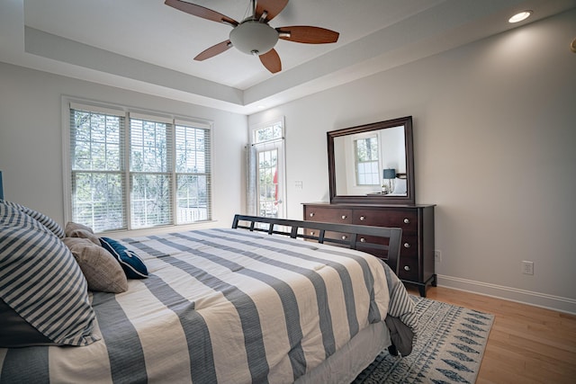 bedroom featuring ceiling fan, baseboards, a raised ceiling, and wood finished floors