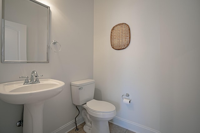 half bathroom with toilet, baseboards, a sink, and tile patterned floors