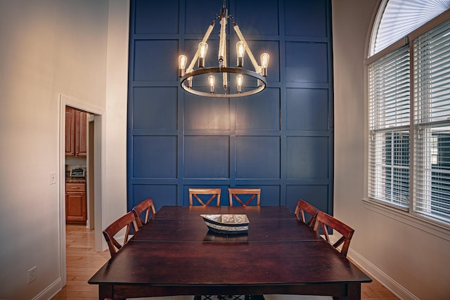 dining space with a chandelier, a decorative wall, baseboards, and wood finished floors