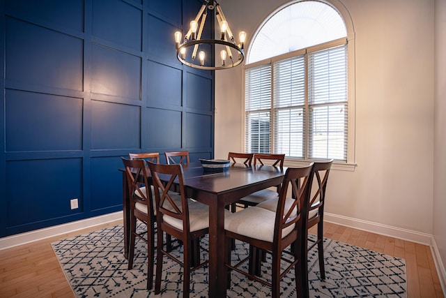 dining room with baseboards, light wood finished floors, an inviting chandelier, and a decorative wall