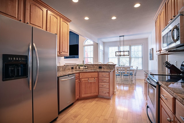 kitchen with appliances with stainless steel finishes, dark stone counters, a sink, and light wood finished floors