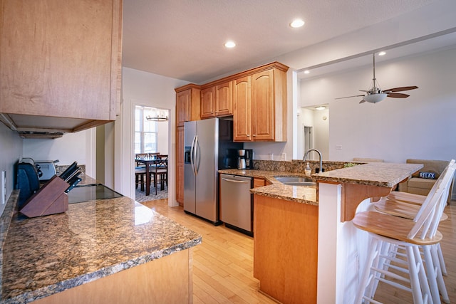 kitchen with a breakfast bar area, stainless steel appliances, a sink, light stone countertops, and a peninsula