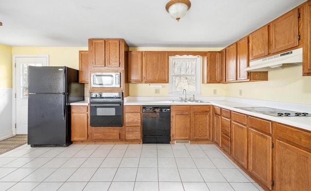 kitchen featuring light countertops, brown cabinetry, a sink, under cabinet range hood, and black appliances