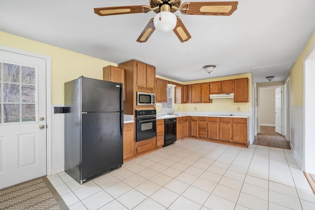 kitchen featuring light tile patterned floors, under cabinet range hood, light countertops, black appliances, and brown cabinetry