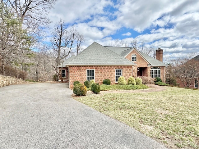 view of front of property with brick siding, a chimney, a shingled roof, driveway, and a front lawn