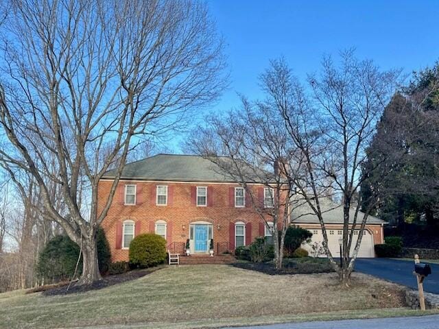 colonial house with a front yard, brick siding, driveway, and an attached garage