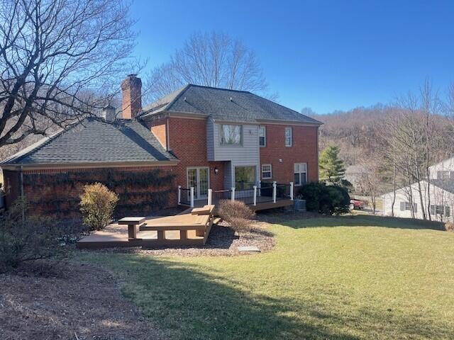 back of property featuring french doors, brick siding, a yard, a chimney, and a wooden deck