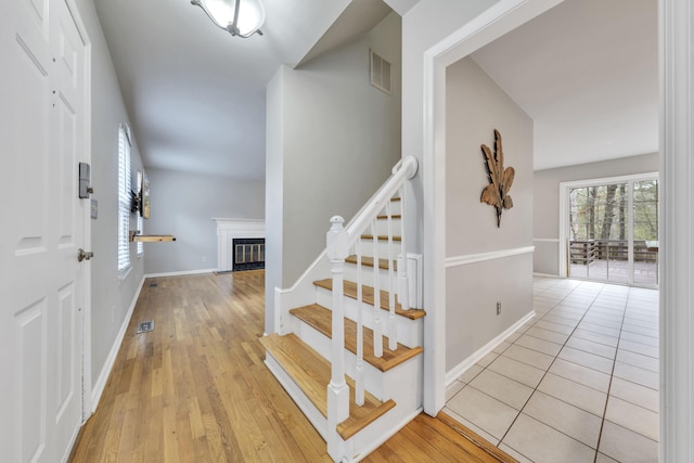 stairs with a glass covered fireplace, visible vents, baseboards, and wood finished floors