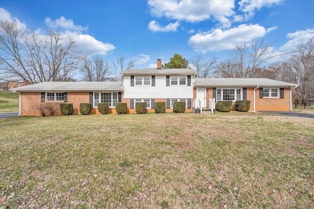 split level home featuring a front lawn, a chimney, and brick siding