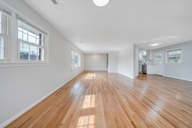 unfurnished living room with stairs, a textured ceiling, light wood-style flooring, and baseboards