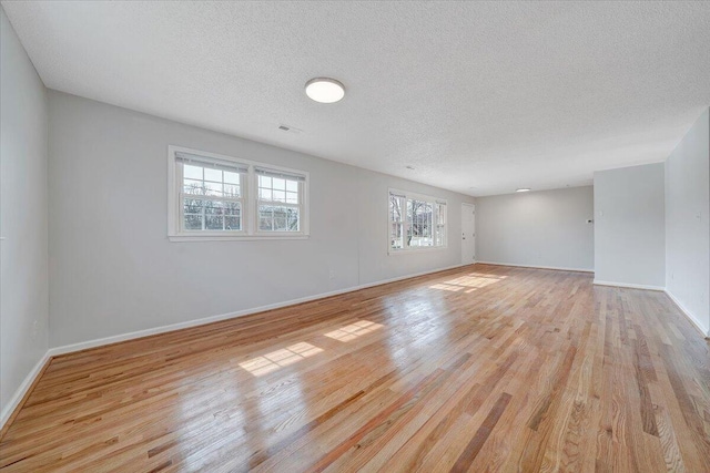 unfurnished room featuring light wood-type flooring, baseboards, visible vents, and a textured ceiling