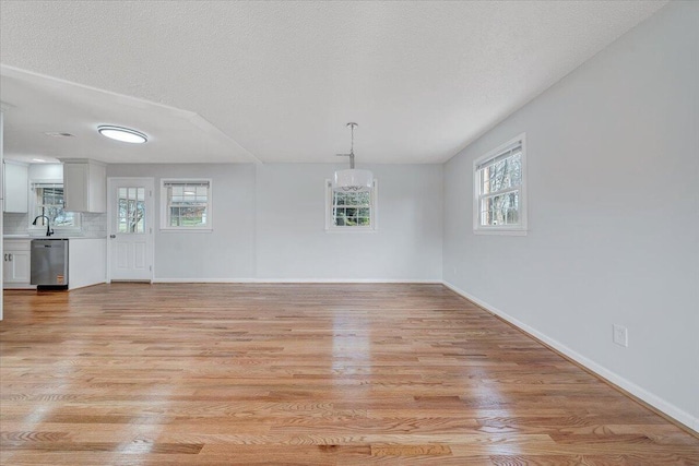 unfurnished dining area featuring light wood finished floors, baseboards, an inviting chandelier, a textured ceiling, and a sink