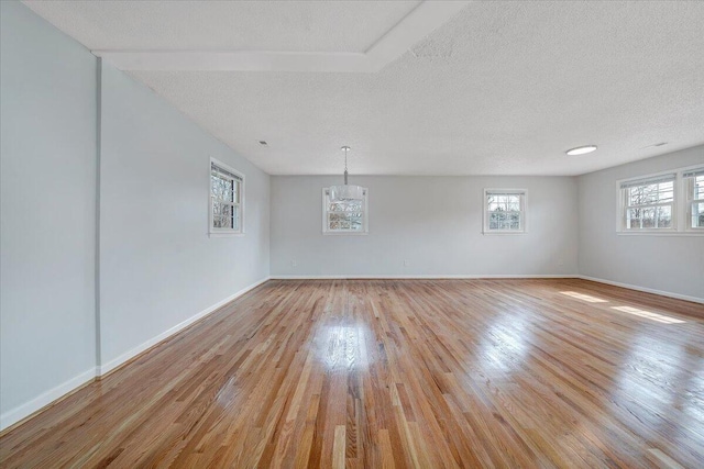 unfurnished room with light wood finished floors, baseboards, and a textured ceiling