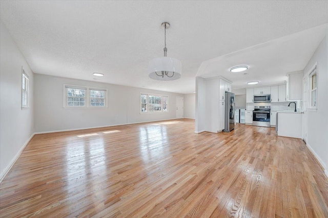 unfurnished living room with light wood-type flooring, a textured ceiling, baseboards, and a sink