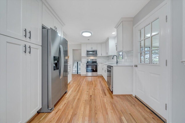 kitchen with tasteful backsplash, light countertops, light wood-style flooring, appliances with stainless steel finishes, and a sink