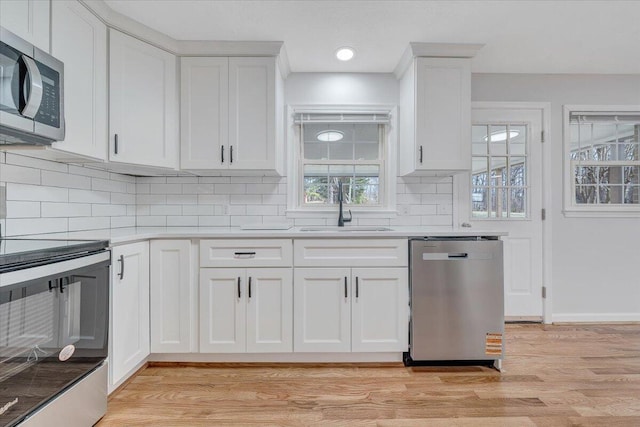 kitchen with a sink, white cabinetry, light countertops, appliances with stainless steel finishes, and light wood-type flooring