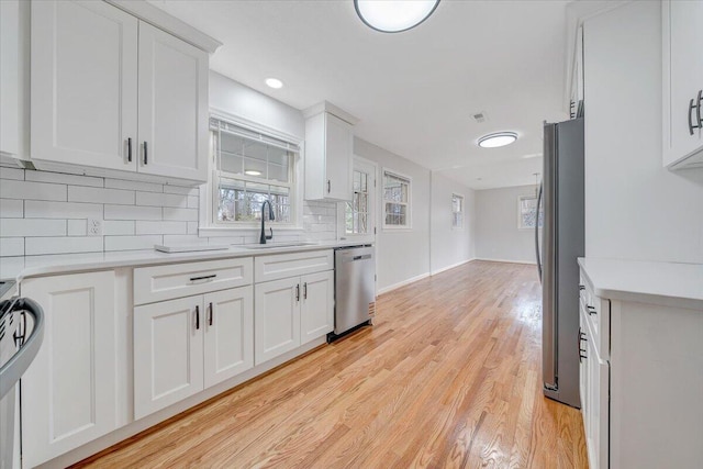 kitchen with a sink, white cabinets, appliances with stainless steel finishes, light wood-type flooring, and tasteful backsplash