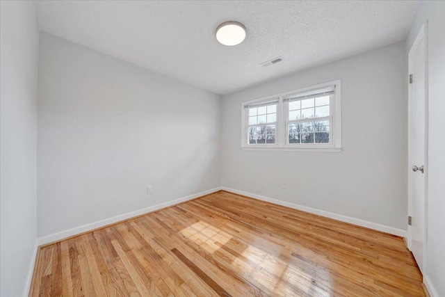 unfurnished room with visible vents, a textured ceiling, baseboards, and wood finished floors