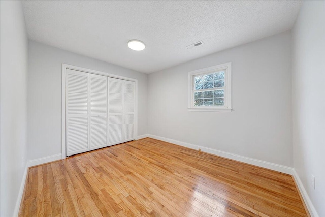 unfurnished bedroom with a textured ceiling, visible vents, baseboards, a closet, and light wood-type flooring