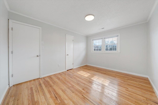 unfurnished room with a textured ceiling, light wood-style flooring, visible vents, baseboards, and crown molding